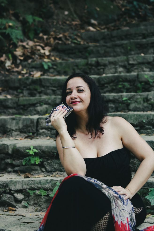 cartomante camilla carvalho sentada em uma escada segurando o baralho cigano